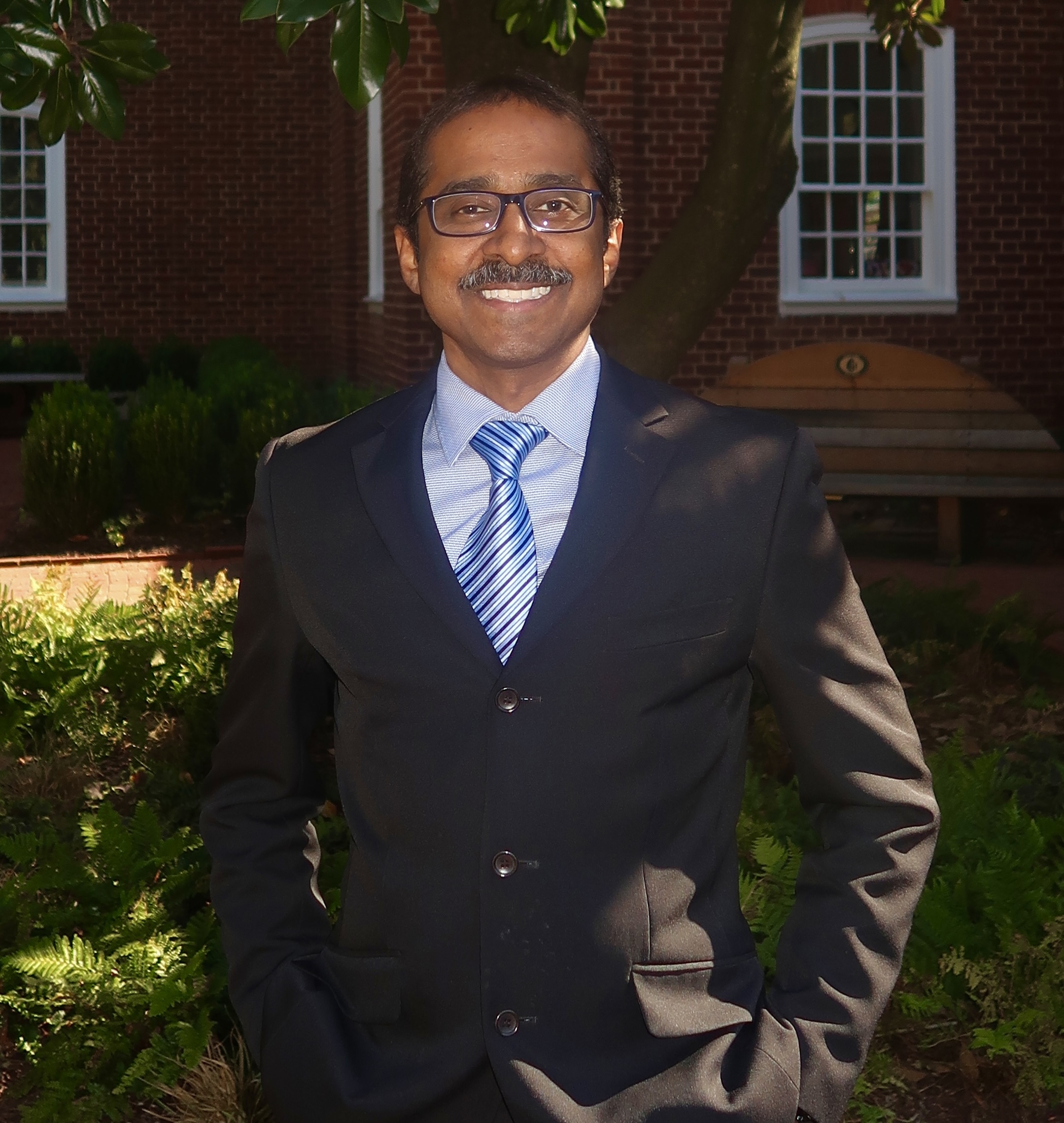 Jay Arasan,  Director, smiling in front of a global map